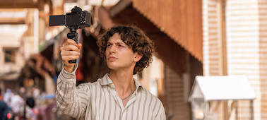 Usage image of a man holding a grip attached to the camera in his right hand, filming himself walking down the street