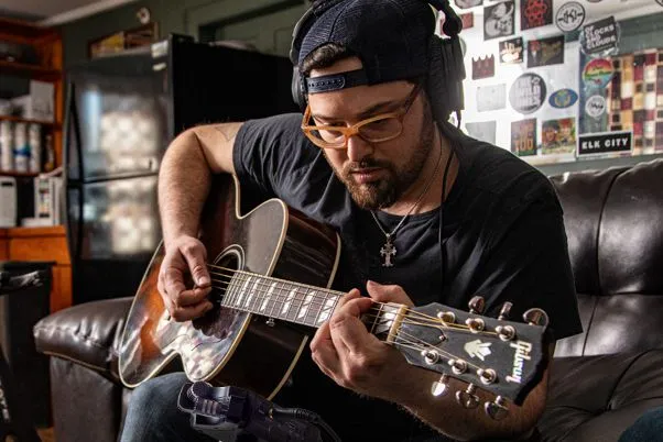 Michael Mazzaraco playing an acoustic guitar in a living room, recording to an H4n Pro